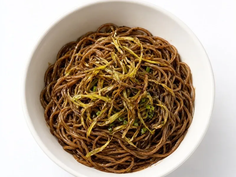 Bowl of dark soy-tossed noodles topped with crisp fried scallion strips.
